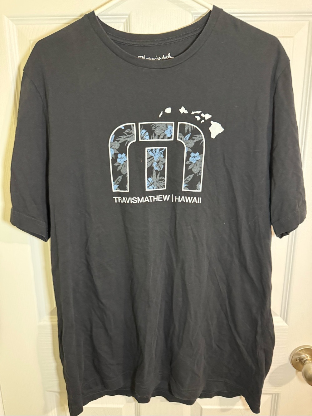 Travis Mathew Hawaii Black Short-Sleeve Logo Tee with Blue Floral Accent